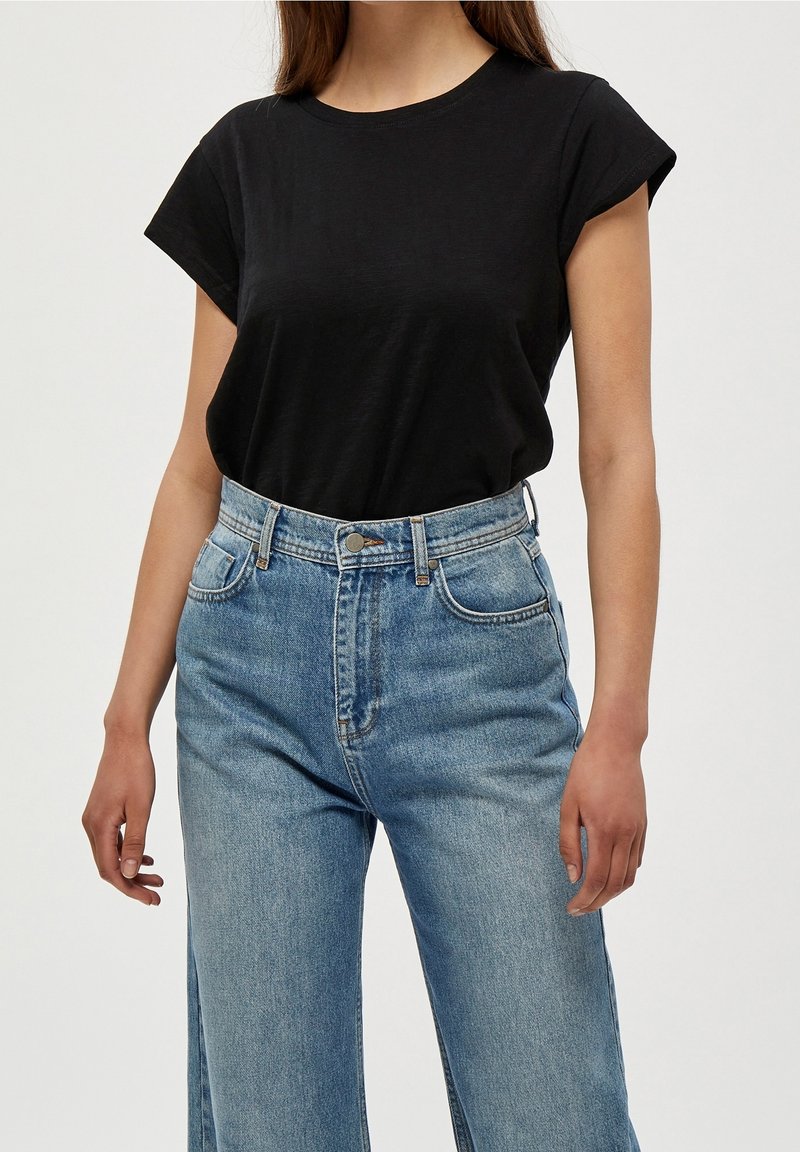 Černé tričko s krátkými rukávy a kulatým výstřihem, doplněné o světle modré džíny s vysokým pasem, volným střihem a rovnými nohavicemi.