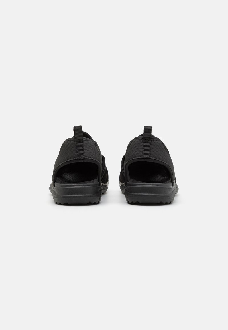 Zwarte sandalen met open hielen, bovenwerk van textuurstof, verstevigde hak en rubberen zool met een profiel voor grip. Twee trekflappen bij de hak.