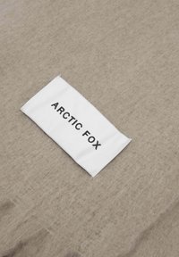 Tissu en feutre beige avec une étiquette d'entretien blanche portant l'inscription « ARCTIC FOX » en texte noir, montrant une texture douce et un design simple.