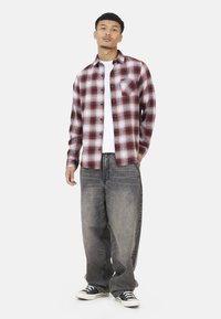 Czerwono-biała koszula w kratę z flaneli, w połączeniu z luźnymi szarymi dżinsami i czarnymi trampkami. Posiada kieszonkę na piersi i zapięcie na guziki.