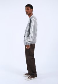 Gray cardigan with white zigzag pattern, paired with dark brown pants and brown sneakers. Cardigan features button closure and ribbed cuffs.
