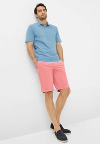 Lyseblå polo-shirt med krave, parret med lyserøde shorts og mørke slip-on sko. Outfittet har en afslappet, løs pasform.