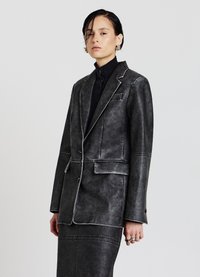 Blazer in similpelle grigia texturizzata con cuciture a contrasto bianche, rever appuntiti e due tasche frontali abbinato a una gonna coordinata.