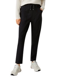 Black trouser pants with an elastic waist and drawstring, featuring side pockets, a straight fit, and clean stitching details. Paired with white sneakers.