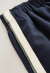 Granatowe bawełniane spodnie z elastycznym pasem, z kremowym paskiem bocznym wykończonym oliwkową zielenią. Gładka tekstura, casualowy design.