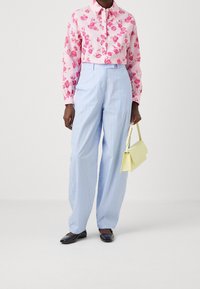 Camicia a bottoni con stampa floreale rosa, pantaloni a righe blu chiaro a gamba larga, ballerine nere e una borsa strutturata gialla.