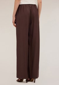 Pantalons larges marron avec une finition texturée, dotés d'une ceinture élastique et d'un long tombé, associés à des sandales à talons hauts marron.