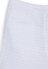 Tessuto bianco testurizzato con tasca orizzontale e vita elasticizzata, che mostra dettagli ravvicinati del motivo di tessitura.