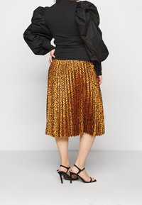 Top nero a coste con maniche a sbuffo abbinato a una gonna plissettata con stampa leopardata arancione e marrone. Sandali neri con tacco a spillo completano l'outfit.