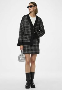 Mustvalge ruuduline kootud kardigan kahe esikoti ja sobiva seeliku paariga. Aksessuaarideks on hõbedane käekott ja mustad saapad.