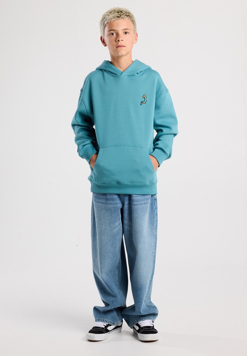 Teal hoodie made of soft fabric with a kangaroo pocket and an embroidered accent. Paired with wide light blue jeans and black sneakers.