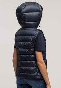 Granatowa kamizelka puchowa z kapturem, z pikowanym wzorem i zapięciem na zamek z przodu. Błyszczący, gładki materiał nadaje elegancki wygląd.