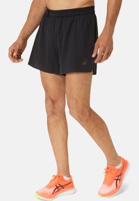 Black athletic shorts with a lightweight, textured fabric; features a side-slit design. Paired with bright orange running shoes.