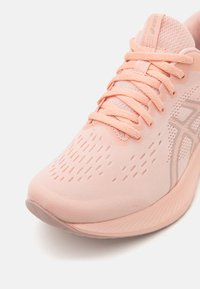 Light pink athletic shoe with a textured mesh upper, prominent lacing system, and a flexible sole featuring subtle ridges and gentle curves.