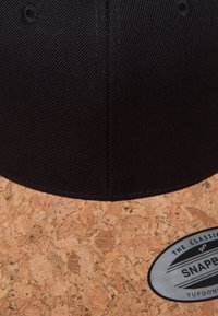 Fekete szövet felsőrész, parafa peremmel, fémből készült snapback záródással és bal oldalon elhelyezett címkével.