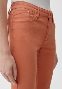 Pomarańczowe jeansy bawełniane o dopasowanym kroju, z pięcioma kieszeniami i subtelnymi detalami przeszycia. Gładka faktura, średni stan.