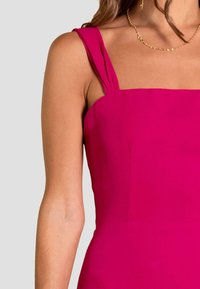 Vestido magenta ajustado con escote cuadrado, tirantes gruesos con acentos pliegues y una textura de tela suave. Primer plano de la parte superior.