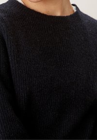 Czarny sweter z dzianiny o okrągłym dekolcie i ribbowanej fakturze. Tkanina wydaje się miękka, prezentując luźną konstrukcję dzianiny.