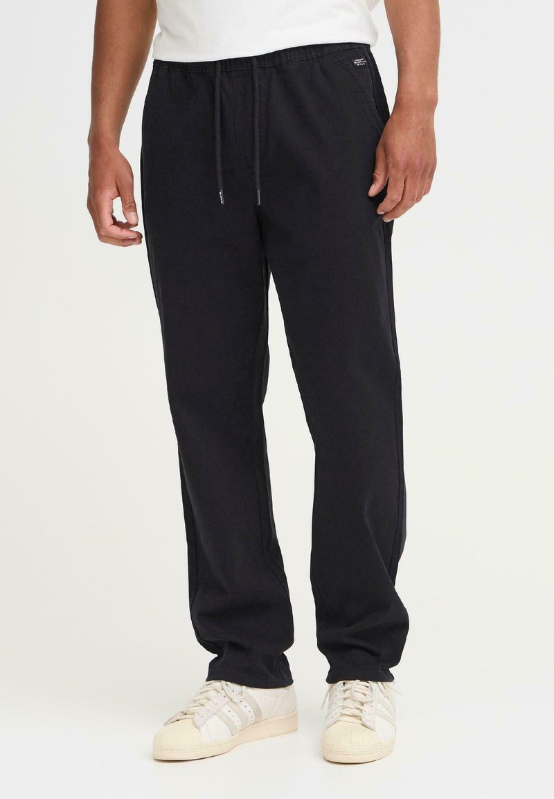 Pantalones jogger de algodón negros con cintura elástica, cordón, bolsillos laterales y un ajuste relajado, combinados con zapatillas blancas.