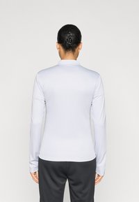 Μακρυμάνικη ανοιχτογκρι πόλο μπλούζα με γιακά, λεία υφή και εφαρμοστή σχεδίαση, σε συνδυασμό με μαύρο παντελόνι, φαίνεται από πίσω.