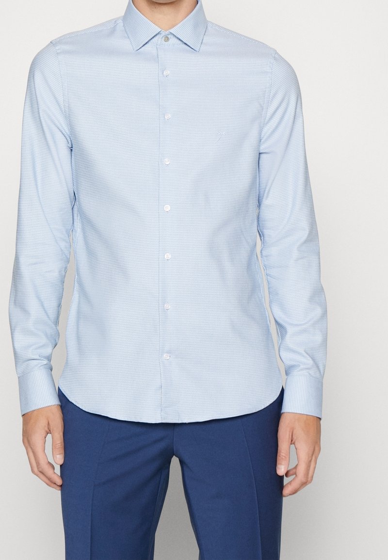 Light blue button-up shirt with a subtle check pattern, long sleeves, and a pointed collar. Features white buttons along the front.