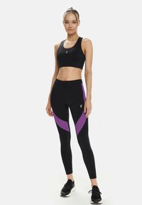 Black sports bra and leggings with purple curved accents. Leggings feature a high waist and contrasting panel design. Textured, stretchy material.