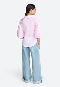 Camicia rosa chiaro con maniche a sbuffo, dettagli con bottoni sulla schiena. Abbinata a jeans in denim azzurro a gamba larga con orlo arrotolato.