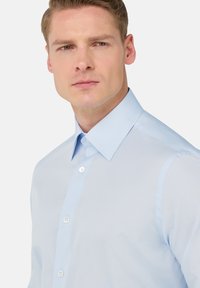 Camicia azzurro chiaro con colletto strutturato, sottili righe verticali e bottoni bianchi. Texture del tessuto liscia.