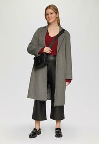 Grijze wolcoat, oversized pasvorm, gecombineerd met een bordeaux ribbeltop en zwarte neplederen wijde broek. Zwarte schoudertas en schoenen.