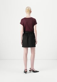Burgunderfarget kortermet topp med rulletermer, kombinert med et svart, høyt liv skjørt. Modellen har på seg svarte slingback hæler.