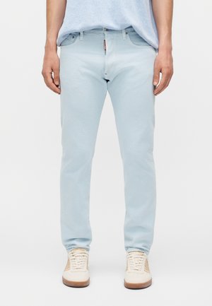 Άτομο που φοράει ανοιχτόχρωμο τζιν και λευκά αθλητικά παπούτσια, στέκεται με τα χέρια χαλαρά στο πλάι σε λευκό φόντο.