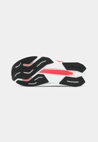 Semelle de chaussure de course en noir et blanc, présentant une texture anti-dérapante, des crampons bien visibles et des accents rouges pour l'adhérence et le soutien.