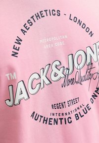 Pink stof med sort og hvid tekst, herunder "Jack & Jones," "New Aesthetics - London," og "Authentic Blue Denim."