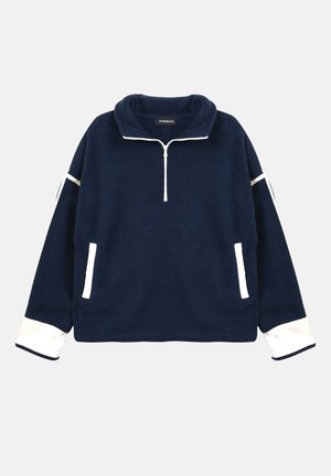Pull-over en polaire bleu marine avec une fermeture éclair blanche au quart, des poignets blancs et des bords blancs sur les poches et les manches, posé à plat sur un fond clair.