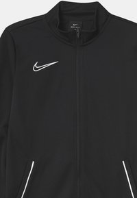 Chaqueta negra Nike Dri-FIT con cuello alto, cremallera completa, logotipo blanco en el pecho y dos bolsillos laterales con ribete blanco. Tejido liso y texturizado.