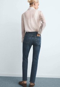 Džiny s vysokým pasem v tmavě modré barvě, slim fit, se dvěma zadními kapsami a mírným vyblednutím; v kombinaci se světle pruhovanou košilí s dlouhým rukávem.