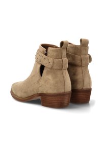 Botas de tobillo de ante beige con punta redondeada, recortes laterales y un detalle de correa con tachuelas, que cuentan con un tacón apilado.