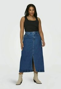Saia maxi de ganga com uma fenda frontal, apresentando uma cintura alta, dois bolsos frontais e um tom de azul claro. Combinada com uma blusa preta sem mangas e botas bejes.