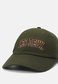 Olivengrønn bomulls baseball cap med buet skjerm og brodert "LES DEUX" i lilla og gull skrift på fronten.