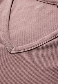 Top s V-výstrihom, ryhovaný v tlmenej fialovej farbe. Má jemnú, textúrovanú tkaninu s jemným leskom. Kvalitne prešitý detail výstrihu.