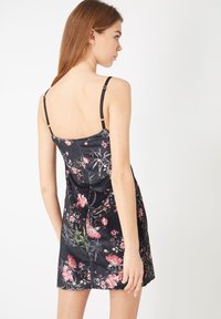 Vestido negro con estampado floral, de tirantes finos y un vibrante patrón floral en rosa y verde. Tejido suave con un diseño ajustado y una abertura en la parte trasera.