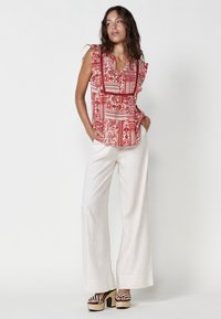 Blusa a maniche ruffle a motivi rossi e bianchi, abbinata a pantaloni a gamba larga beige chiaro e sandali con plateau in bianco e nero.