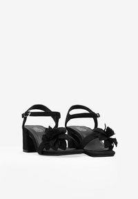 Sandalias de tacón de ante negro con un acento de flor, correa de tobillo ajustable, diseño de punta abierta y un tacón grueso para mayor estabilidad.