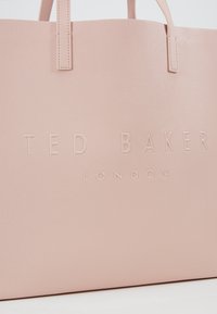 Sac fourre-tout rose texturé avec logo embossé "TED BAKER LONDON." Doté de deux anses et d'un intérieur spacieux. Design minimaliste et finition douce.