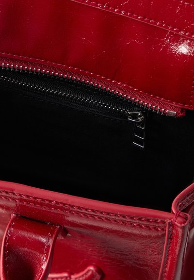 Κόκκινη δερμάτινη τσάντα με ορατή λεπτομερή ραφή και μαύρη εσωτερική τσέπη με φερμουάρ, εν μέρει ανοιχτή.