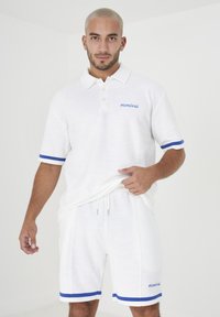 Polo shirt bianco con accenti blu e ricamo "mcmxlii", abbinato a pantaloni corti bianchi con orli a righe blu. Tessuto morbido e strutturato.