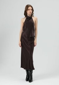 Bruin satijnen haltertop met een vloeiende silhouet en gelaagde zoom, gecombineerd met een bijpassende lange rok en zwarte hoge hakken.