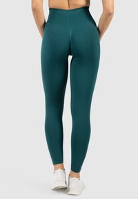 Hochtaillierte türkisfarbene Leggings mit einem strukturierten Rautenmuster, passgenauer Form und nahtloser Verarbeitung. Getragen mit weißen Sportschuhen.
