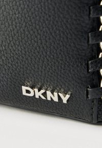 Μαύρο πορτοφόλι από δερμάτινη υφή με ασημένιο λογότυπο "DKNY" και περίτεχνη υφαντή λεπτομέρεια κατά μήκος της άκρης.