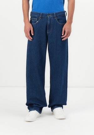 Blauwe denim jeans met een relaxed fit, voorzien van vijf zakken, een knoopsluiting en subtiele stikseldetails. G gedragen met witte sneakers.